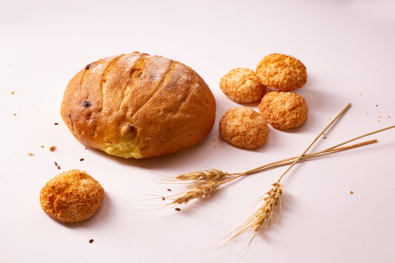 Close-up of homemade bread loaf and cookies with wheat on a light background.