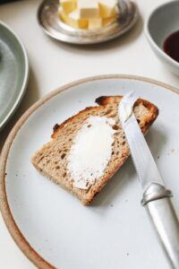 A close-up of buttered bread with a knife on a ceramic plate, perfect for a breakfast scene.