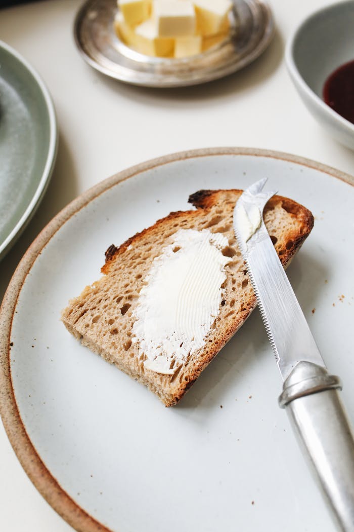 A close-up of buttered bread with a knife on a ceramic plate, perfect for a breakfast scene.