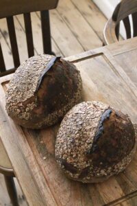 Freshly baked sourdough bread loaves with oats on a rustic wooden table.